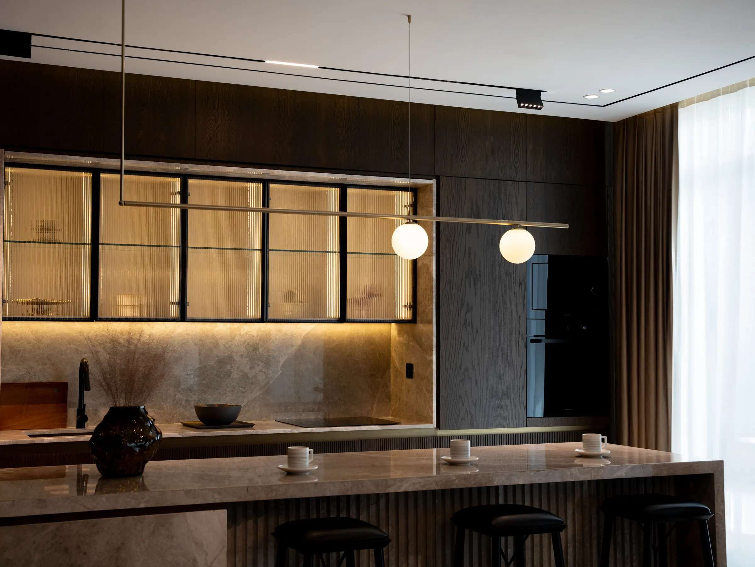 Dark walnut modular kitchen with fluted glass wall units, warm under-cabinet lighting and stone island